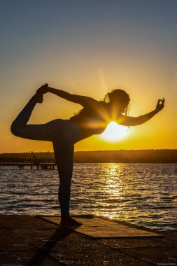 Sarışın bir kadın gün batımında gölün kenarında yoga pozu veriyor. Vücut sağlığı. Yaşam biçimi.