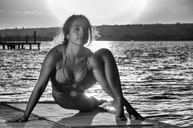 Sarışın bir kadın gün batımında gölün kenarında yoga pozu veriyor. Vücut sağlığı. Yaşam biçimi.