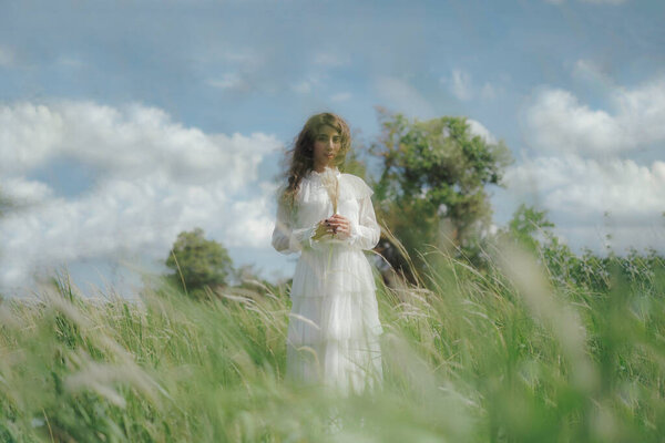 Portrait of woman in white dress standing in meadow againt blue sky and white cloud, looking at camera, holding fountain grass.