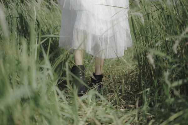 Close up of woman in white dress and black boot walking in the meadow, summer is coming, freedom, concept.
