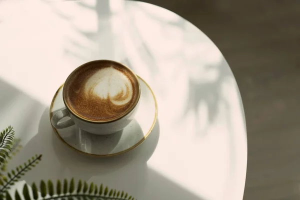 Köşesinde Bulanık Eğreltiotu Yaprağı Olan Bir Fincan Kahve Beyaz Masaya — Stok fotoğraf