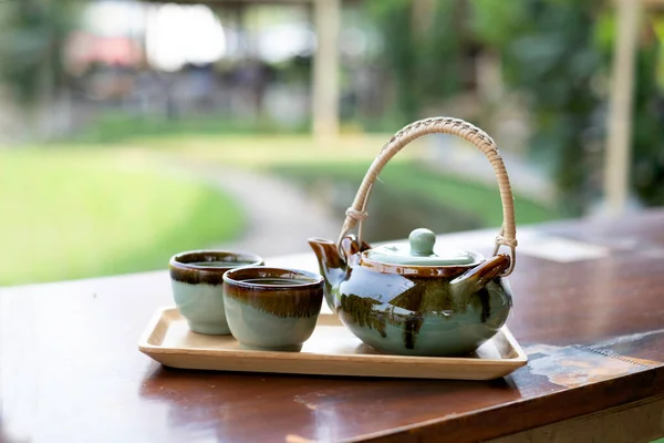 木制托盘和木桌上的绿褐色茶壶和茶杯 背景模糊不清 — 图库照片