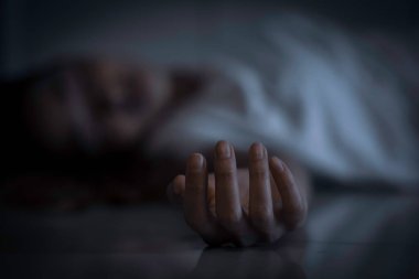 Evdeki Asyalı kadının cesedinin elini kapat. Bulanık beyaz gömlekli kız yere uzanmış, koyu renk tonuyla.