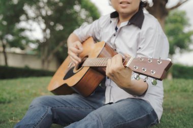 Parkta gitar çalan adamı kapat, yeşil bokeh arkaplan ile kabloya basılmış parmağa odaklan. Rahatlatıcı, doğada müzikle stres atmak..