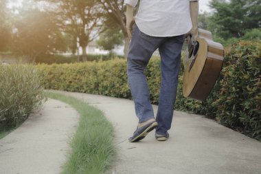 Gitar çalan bir gitarist turuncu ışıkla parkta yürürken.