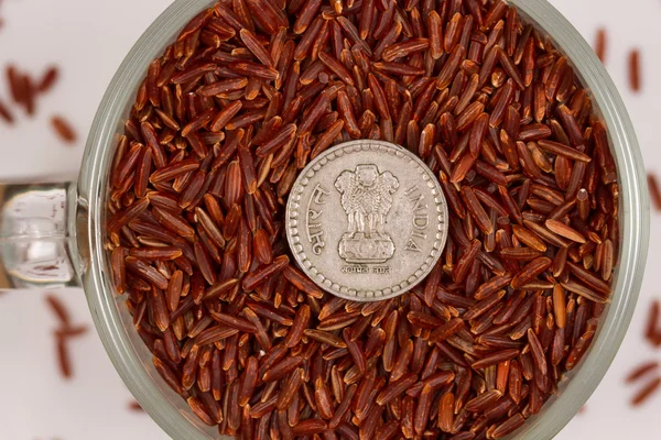 Riso rosso selvatico in una tazza di vetro e rupie indiane . — Foto Stock