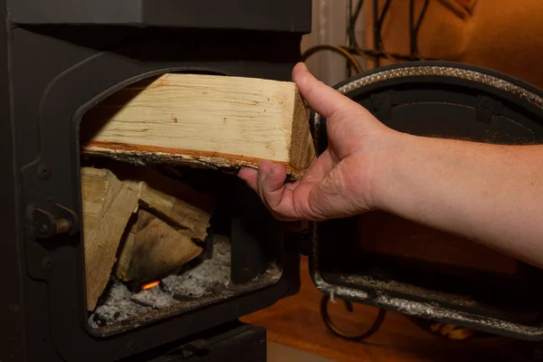 Man puts a firewood in a wood stove — Stock Photo, Image