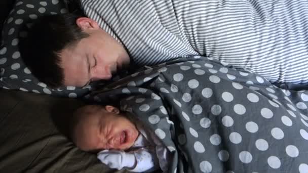 Ein Neugeborenes weint, während es bei seinem schlafenden Vater liegt — Stockvideo