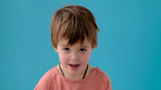 Ragazzo con i capelli biondi annuisce testa in posa contro parete azzurra — Video Stock