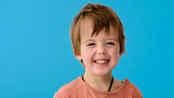 Liten pojke i orange t-shirt leenden på turkos bakgrund — Stockfoto