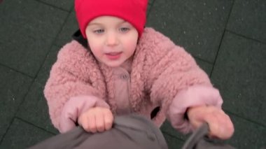 Pembe ceketli ve kırmızı şapkalı kız babasının düğmelerini açıyor.