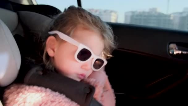 Dziewczyna w okularach przeciwsłonecznych i kurtce śpi w foteliku dla dziecka — Wideo stockowe