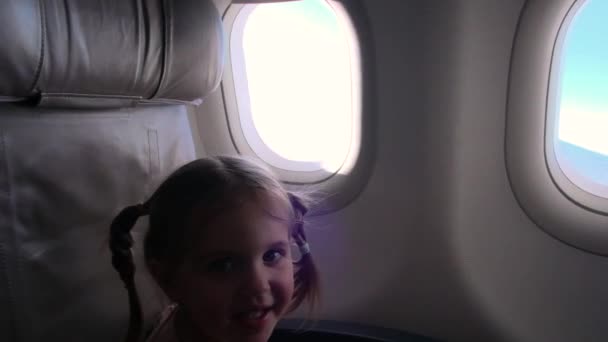 Chica juguetona se sienta en la silla mirando por la ventana en el avión — Vídeo de stock