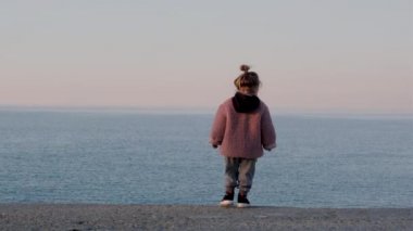 Pembe ceketli tatlı kız sahilden sakin denize bakıyor.