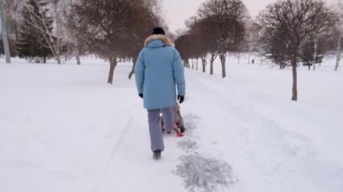 Uzun kışlık montlu yetişkin bir adam küçük bir çocukla kaydırak itiyor.