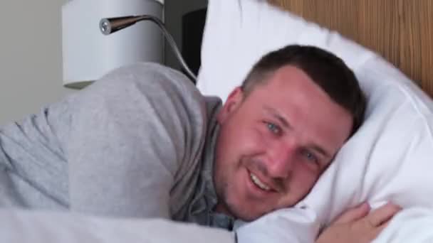 El hombre somnoliento positivo se estira acostado en la cama con almohada grande — Vídeos de Stock