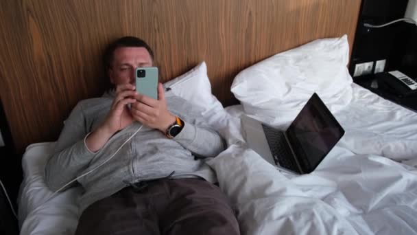 Guy teksty na ładowania smartfona leżącego na łóżku w pokoju hotelowym — Wideo stockowe