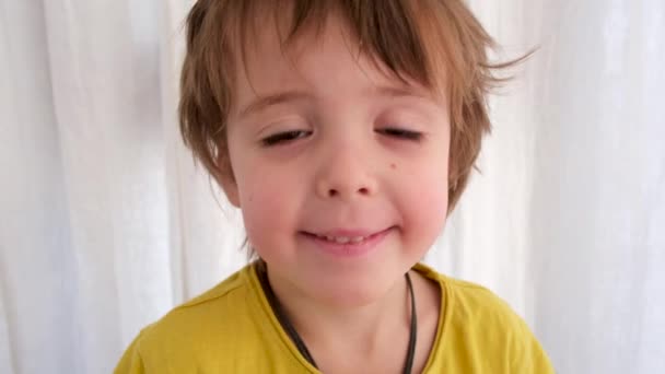 Niño en camiseta amarilla encoge de hombros cerca de la cortina de la ventana — Vídeo de stock