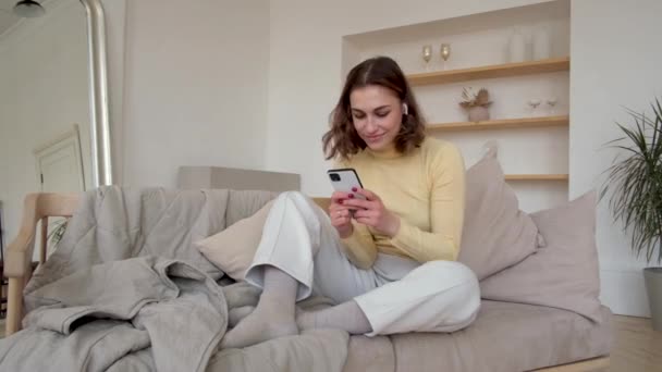 Happy woman with wireless earphones listens to music on sofa — Stock Video