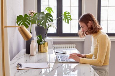 Gülümseyen kız masada oturuyor ve laptopla çalışıyor.