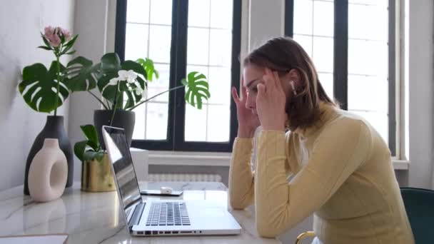 Mujer cansada masajes templos sentado cerca de la computadora portátil en la mesa — Vídeo de stock