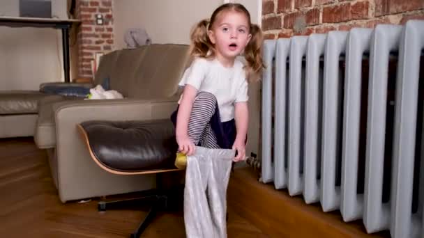 Забавная маленькая девочка надевает блестящие леггинсы, стоящие у радиатора — стоковое видео