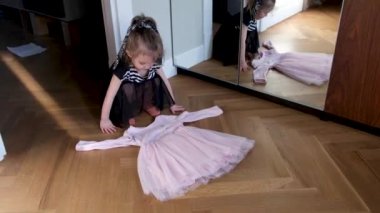 Küçük kız odada büyük aynanın yanındaki pembe elbiseye bakıyor.