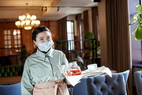 Chelneriță în mască și cu tavă în picioare în cafenea — Fotografie, imagine de stoc