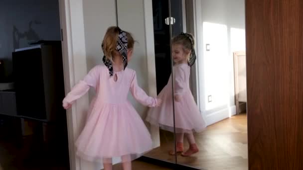 Χαριτωμένο κορίτσι με κοτσίδα φορώντας ροζ φόρεμα χορεύει στον καθρέφτη — Αρχείο Βίντεο