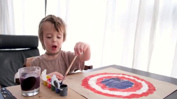 Młody chłopiec rysuje obraz na kartonie z gwasz przy stole — Wideo stockowe