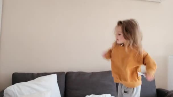 Kleines verdorbenes Mädchen springt auf Sofa in geräumigem Apartment-Zimmer — Stockvideo