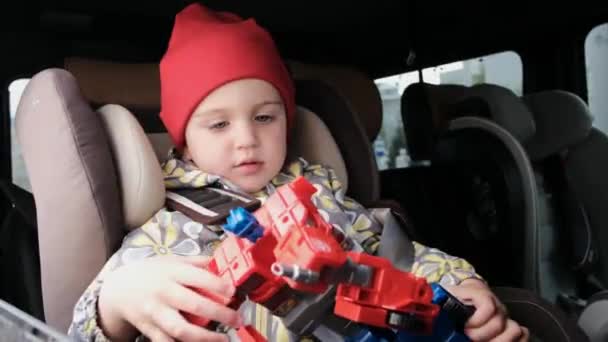 Anak bertopi dan jaket bermain dengan robot duduk di dalam mobil — Stok Video