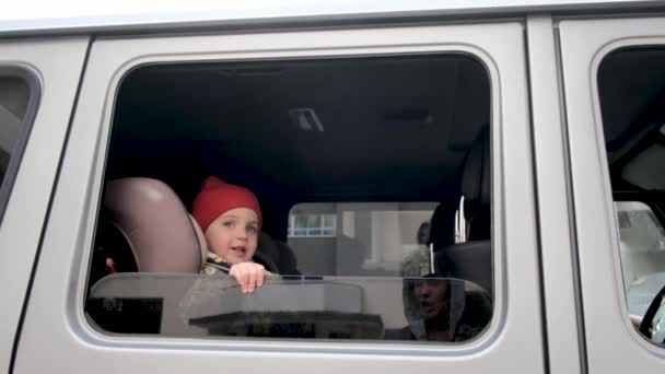 Niño pequeño con sombrero y chaqueta sonríe a la madre sentada en el coche — Vídeos de Stock