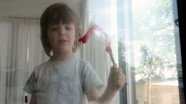 Pojke ritar hjärta med rosa färg och borste på fönsterglas — Stockvideo