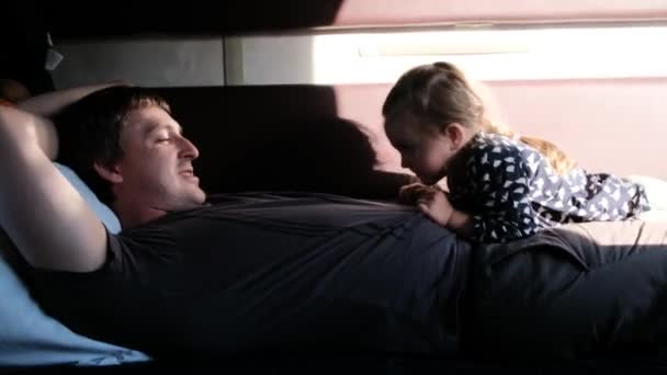 Funny girl kid lies on smiling father and hits dad belly — Stock Video