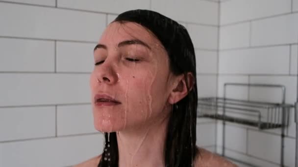 Mulher morena bonita com olhos fechados fica sob jatos de água na unidade de chuveiro — Vídeo de Stock