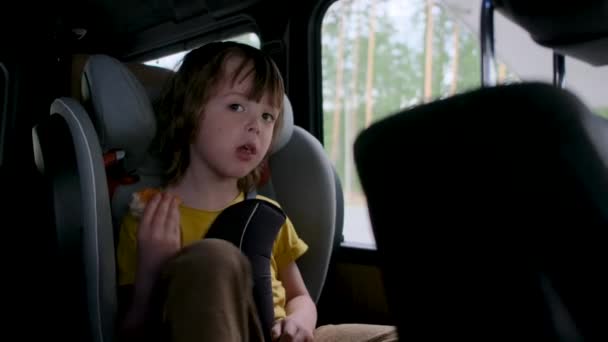 Jeune garçon aux cheveux bruns mange pain grillé dans le siège d'auto — Video