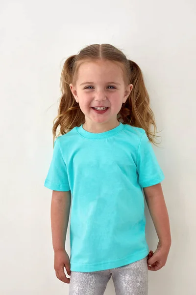 Glad liten flicka i blå skjorta stående i studio — Stockfoto