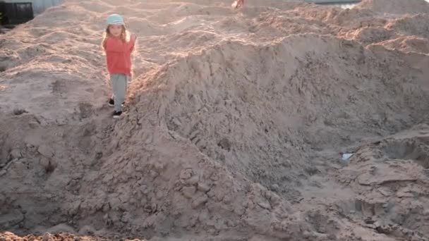 Menina de boné azul e camisola laranja caminha joga em pilhas de areia — Vídeo de Stock