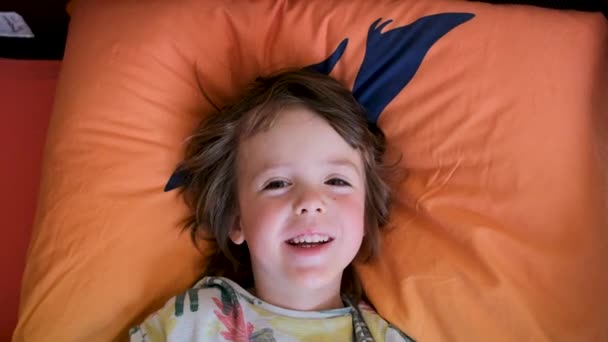 색 티셔츠를 입은 작은 유치원 소년 이 베개 위에 누워 있다 — 비디오