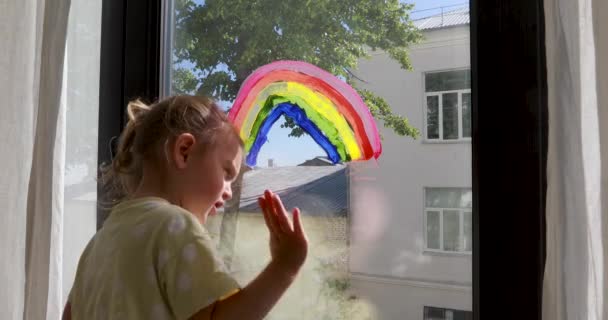 Niña preescolar se para cerca de la ventana con el arco iris colorido — Vídeos de Stock