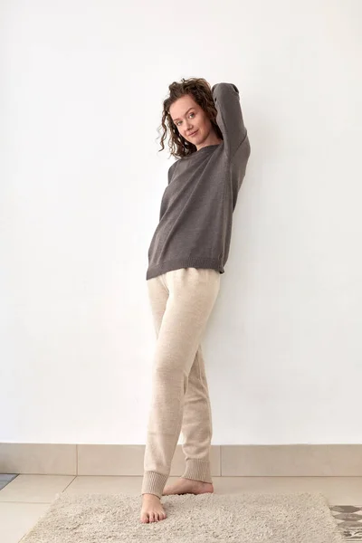 Mujer joven con jersey y pantalones apoyados en la pared blanca —  Fotos de Stock