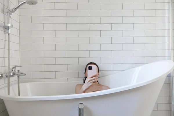 Woman using pink smartphone in white bathtub — Stock Photo, Image