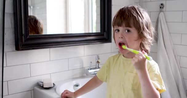 Ένα τετράχρονο αγόρι να βουρτσίζει τα δόντια του σε λευκό μπάνιο. — Αρχείο Βίντεο