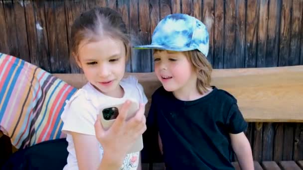 Šťastná dívka s bratrem hodinky video na telefonu v arbor — Stock video