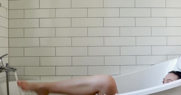 Pełna wdzięku kobieta wyłącza wodę długą nogą leżącą w wannie — Wideo stockowe