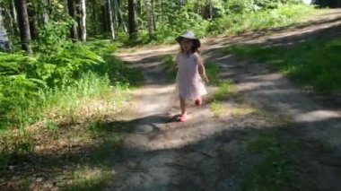 Elbiseli ve şapkalı küçük kız bahar ormanında yol boyunca koşuyor.