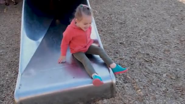 Kleines Mädchen mit Zopf im rosa Kapuzenpulli spielt auf Rutsche im Park — Stockvideo