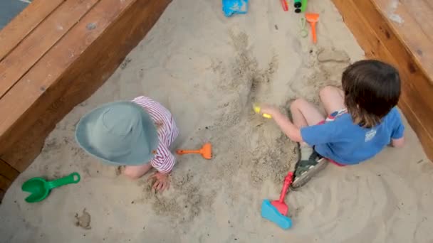 Мальчик копает песок с грабли проводить время с сестрой — стоковое видео