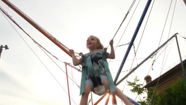 Забавная девушка со светлыми волосами прыгает на батуте среди деревьев — стоковое видео